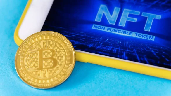 Moeda de Bitcoin física sobre uma tela com o nome NFT